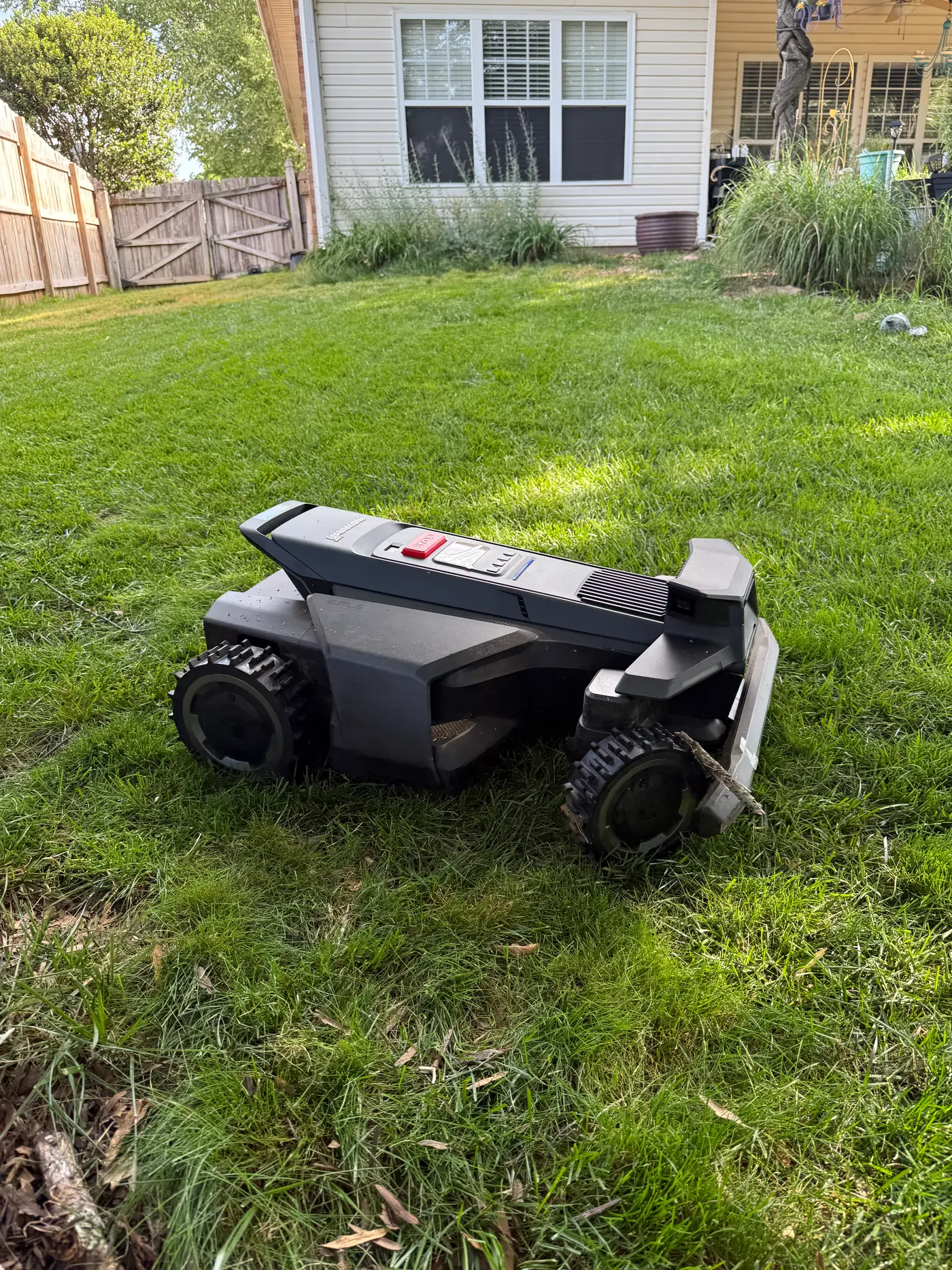 Segway Navimow X430 navigating tall grass on a sloped section near a fence line during first-hand testing — real-world deployment showing the 4WD Xero-Turn AWD system on uneven terrain